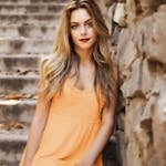Woman Wearing Orange Dress Leaning on Brown Wall Near Stairs